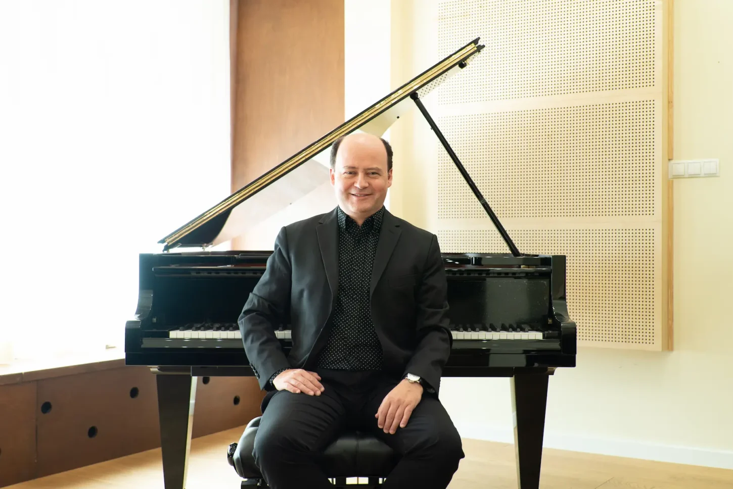 uśmiechnięty Pianista Filip Wojciechowski w ciemnej marynarce siedzi przy otwartym, czarnym fortepianie